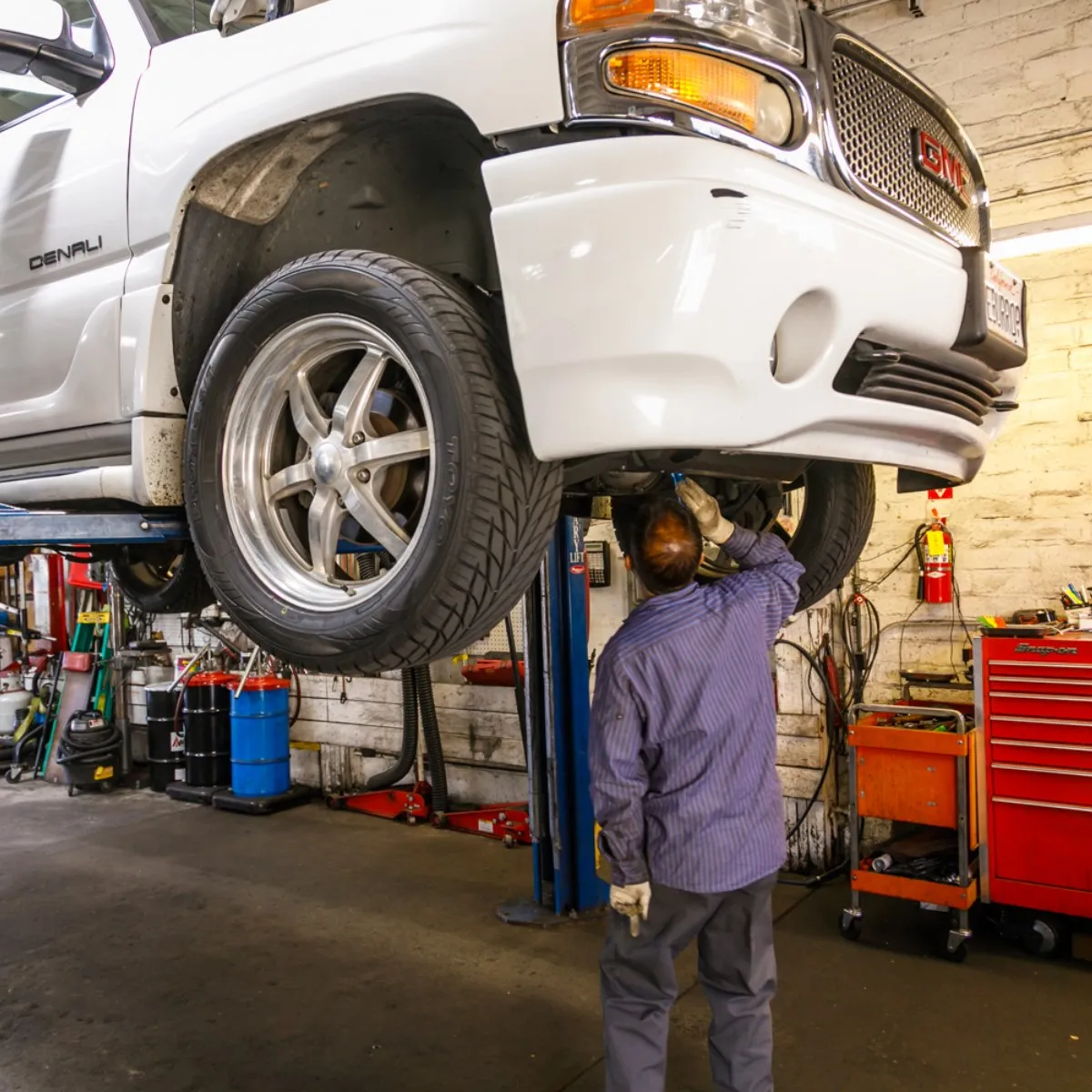 Mechanic inspecting the underside of a white SUV lifted on a hydraulic lift at an auto care shop.